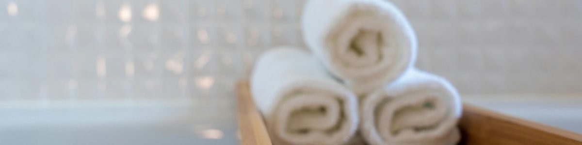 A close-up of rolled white towels on a wooden bath tray in a modern bathroom.