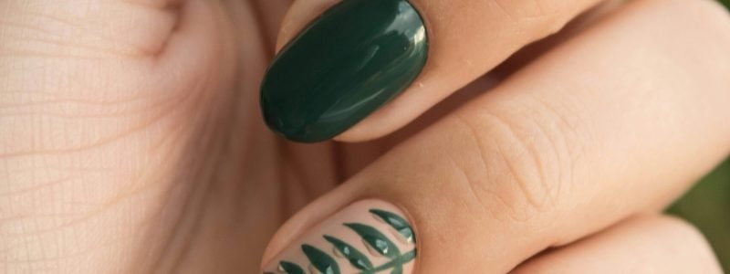 Close-up of a stylish green manicure with a leaf design, showcasing glossy fingernails and natural skin tone.