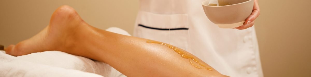 Unrecognizable therapist pouring honey while massaging woman's leg at spa salon.